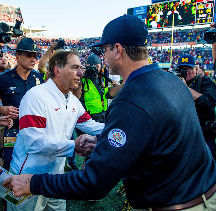 Nick Saban and Jim Harbaugh both lean forward as they shake hands